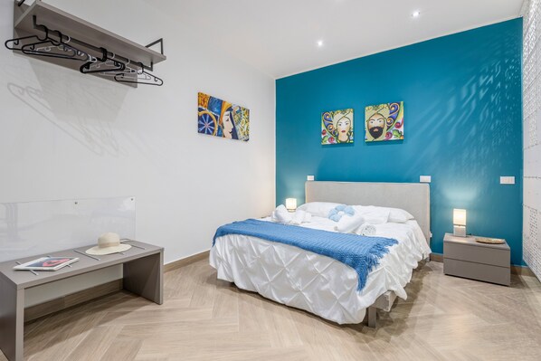 Een moderne slaapkamer met een bed, nachtkastjes, een bureau en kunstwerken aan de wanden.
