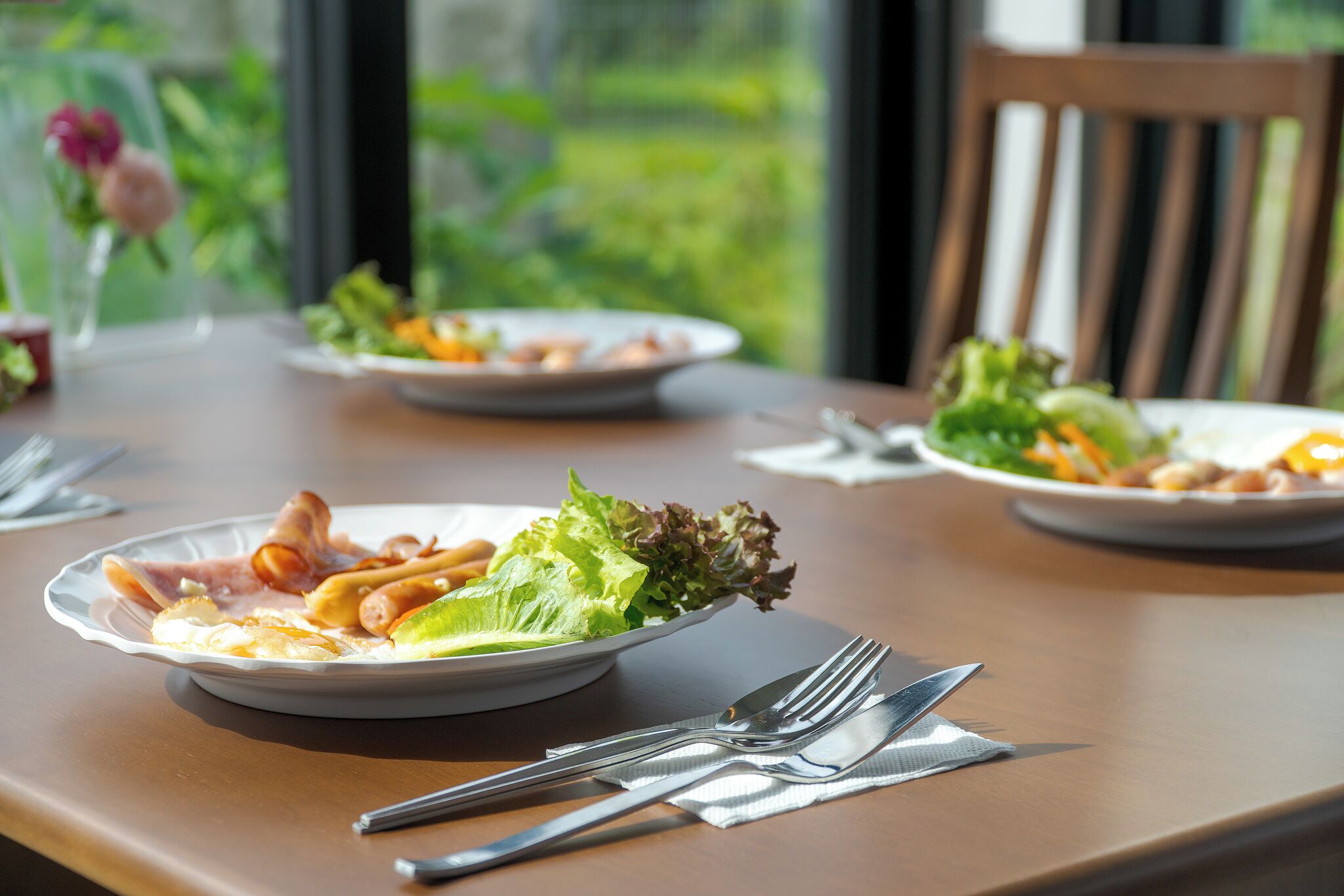 Une table à manger avec des assiettes remplies de nourriture, des couverts et une chaise.