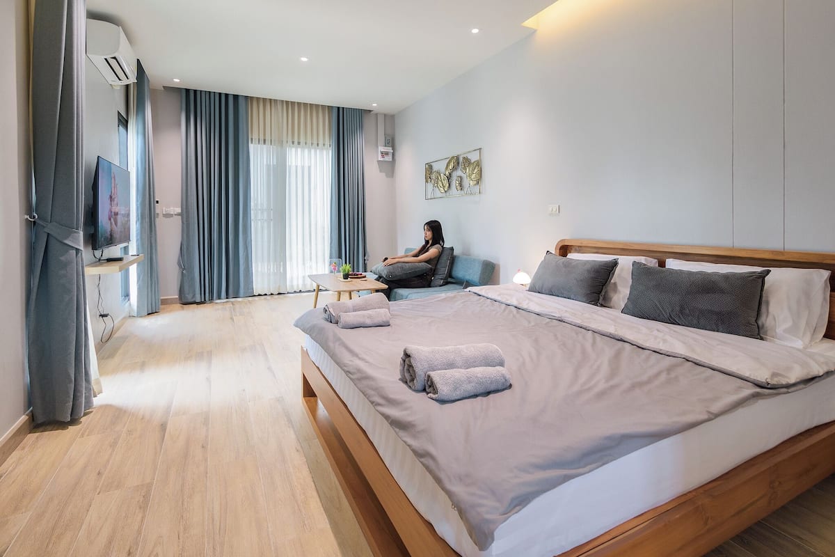 Habitación de hotel moderna con una cama grande, un sofá, un televisor y una ventana con cortinas.