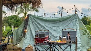 Una carpa montada con una mesa, sillas, una parrilla y luces colgantes.