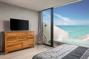 Un dormitorio moderno con un ventanal grande que da a una playa, un aparador de madera y una cama cómoda.