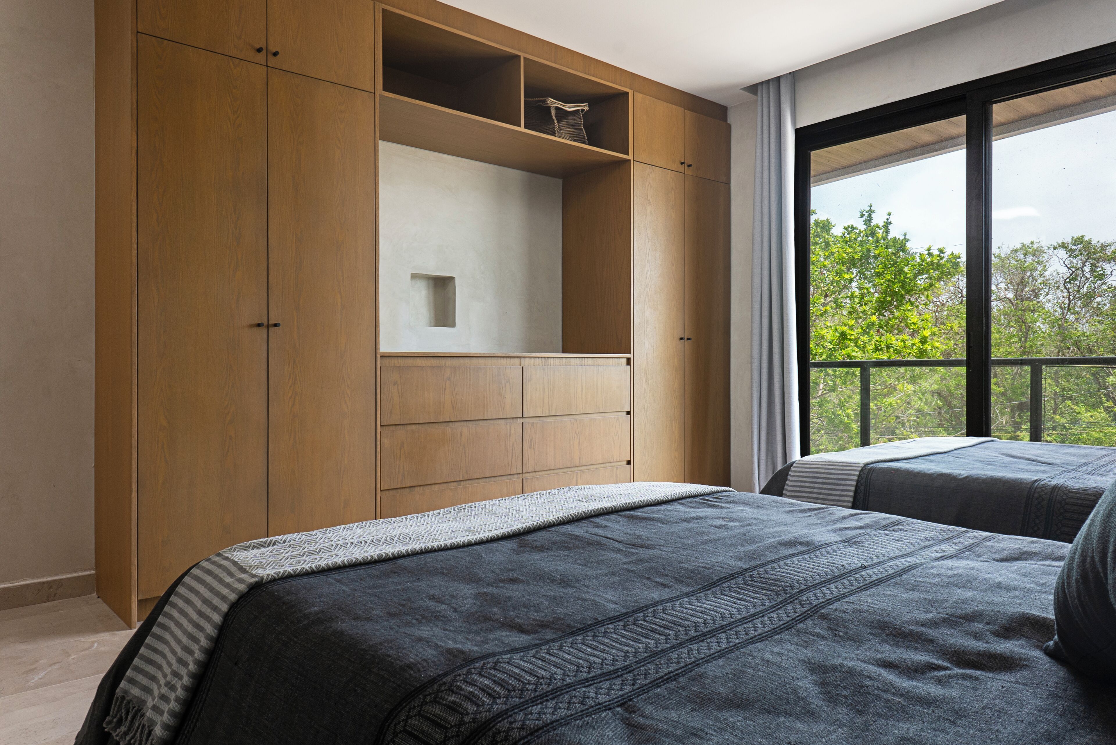 Une chambre avec une grande armoire, deux lits et une fenêtre donnant sur les arbres.
