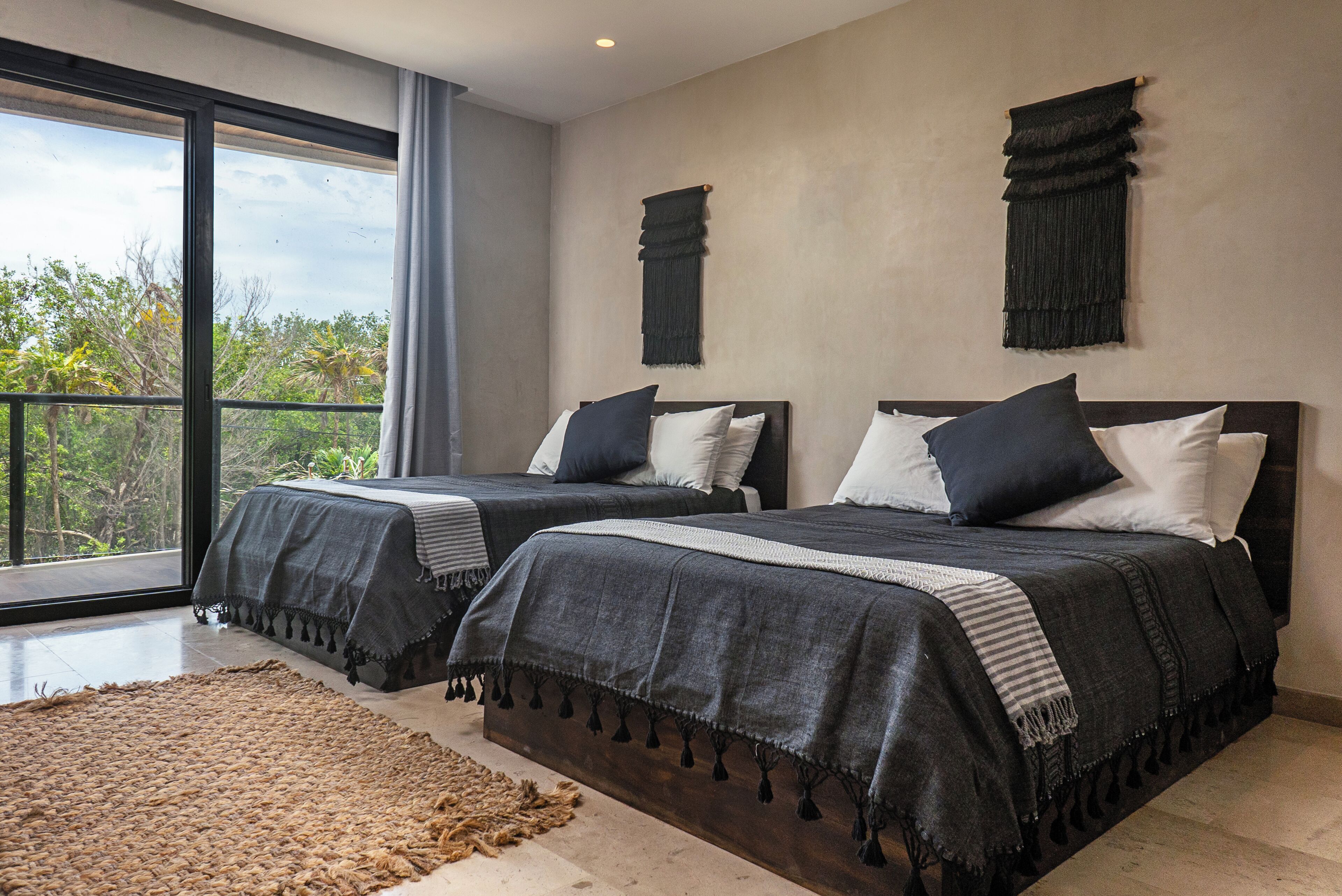 Une chambre moderne avec deux lits, de grandes fenêtres et une vue sur les arbres.