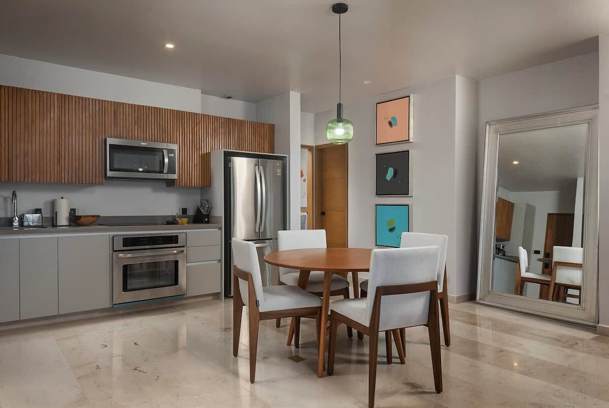 Una cocina moderna con comedor, que incluye una mesa redonda de madera y sillas blancas, un microondas integrado y un refrigerador.