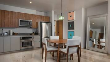 Una cocina moderna con comedor, que incluye una mesa redonda de madera y sillas blancas, un microondas integrado y un refrigerador.