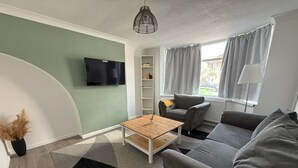 Un soggiorno moderno con un divano grigio, un tavolino in legno, una TV a parete e una finestra con tende.