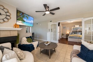 A living room with a fireplace, a television, a ceiling fan, and a bunk bed in the background.