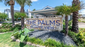 A sign for 'The Palms at Cove View' with a modern building in the background.