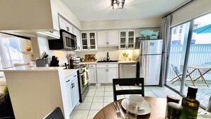 A modern kitchen with white cabinets, a stainless steel refrigerator, and a dining area with a table set for two.