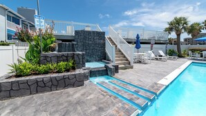 A swimming pool with a stone waterfall feature, white railings, and a sign warning against climbing or sitting on the waterfall.