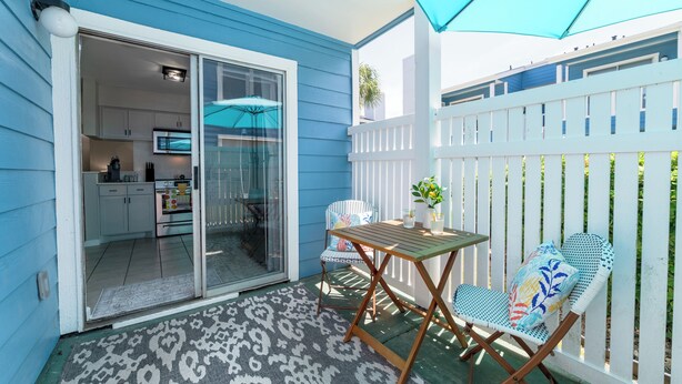 A patio with a table and chairs, a sliding glass door leading to a kitchen, and a white fence.
