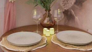 A round dining table with two white plates, two wine glasses, a vase with yellow flowers, and candles. - La Parenthèse Fleurie – Suite with spa and projector screen in Bergerac (Bergerac)
