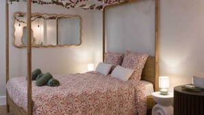 A four-poster bed with floral bedding, a bedside table with a lamp, and a round side table with a book. - La Parenthèse Fleurie – Suite with spa and projector screen in Bergerac (Bergerac)