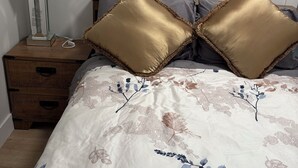 Une chambre à coucher avec une couvre-lit à motifs floraux, une table de chevet en bois avec une lampe et deux coussins dorés.