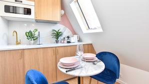 A compact kitchen with wooden cabinets, a white countertop, and a small dining table with blue chairs. - Charming Studio - 2P - Champs Elysees (Paris)
