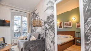 A modern bedroom with a grey sofa, a bed, a large window, and a tropical mural on the wall. - Elegant Apartment - 3br/8p - Gare de L'est (Paris)