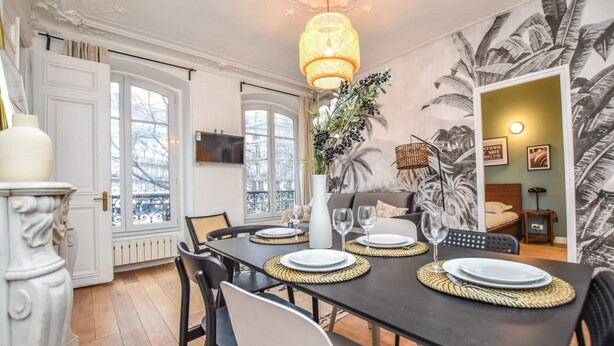 A dining area with a black table set for four, white chairs, a large potted plant, and a wall with a tropical leaf mural. - Elegant Apartment - 3br/8p - Gare de L'est (Paris)