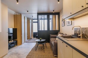 En moderne stue med sofa, fjernsyn og et køkkenområde med vask og bordplade.