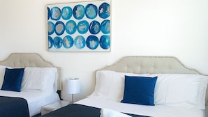 A hotel room with two beds, each with a white and blue bedspread, and a blue and white pillow. There is a painting on the wall above the beds. - The Gathering Place (Kissimmee)