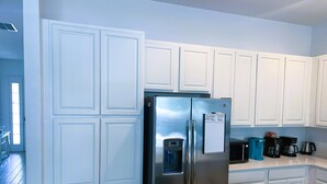 A kitchen with white cabinetry, a stainless steel refrigerator, and a coffee maker. - The Gathering Place (Kissimmee)