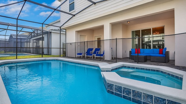 A swimming pool with blue tiles, a glass-enclosed patio with blue lounge chairs, and a gray sofa with red cushions. - The Gathering Place (Kissimmee)