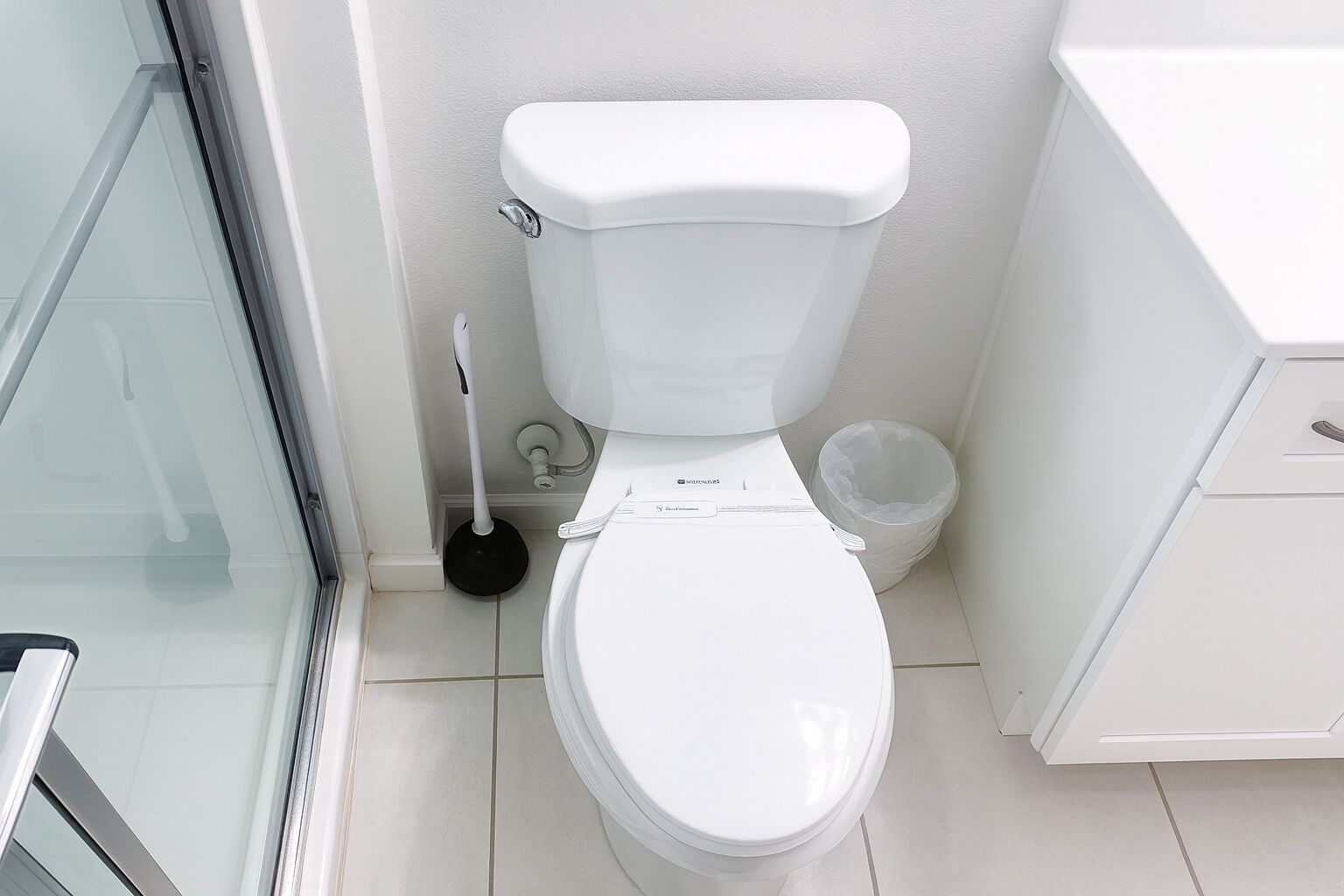 Een moderne badkamer met een wit toilet, een zuignap en een prullenbak.