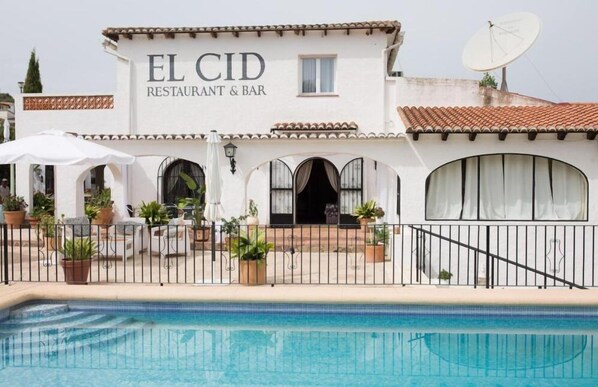 A white building with the sign "EL CID RESTAURANT & BAR" and a swimming pool in front.