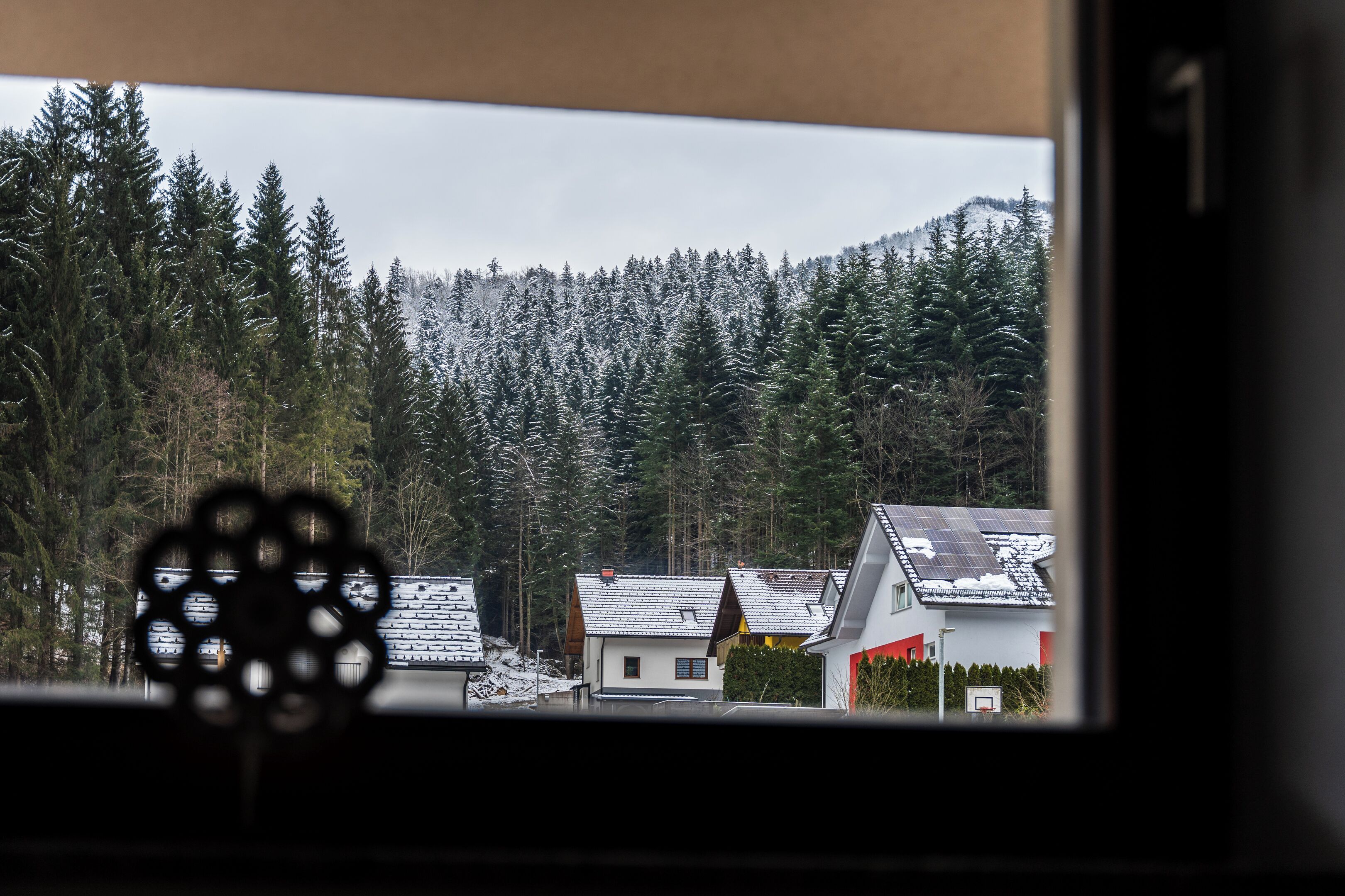 Vista a través de una ventana con una montaña nevada y casas al fondo.
