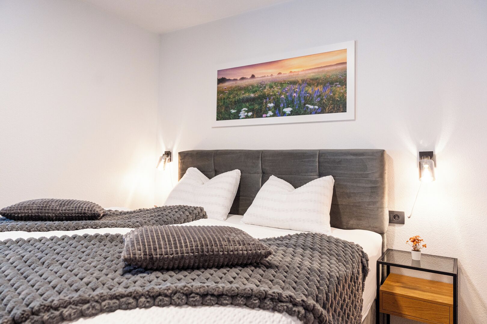 Een slaapkamer met een groot bed, een hoofdeinde, twee nachtkastjes en een wandlamp.