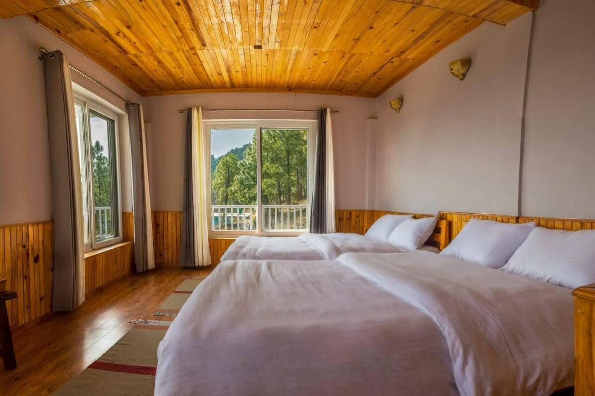 Une chambre avec deux lits, un plafond en bois, de grandes fenêtres et une vue sur les arbres.