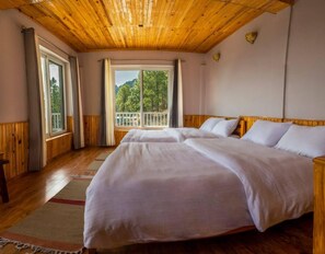 A bedroom with two beds, wooden ceiling, large windows, and a view of trees. - Kasar Rainbow Yoga Retreat (Almora)