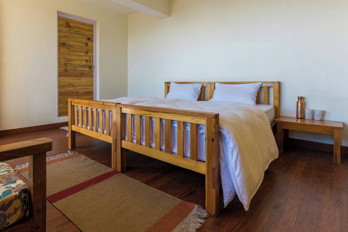 Une chambre à coucher avec un lit en bois, une table de chevet, un banc et une porte dotée d’un panneau en bois.