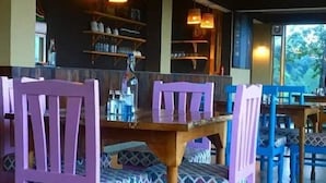 Un comedor con sillas moradas y una mesa de madera, estantes con botellas y copas, y vistas al verdor exterior.