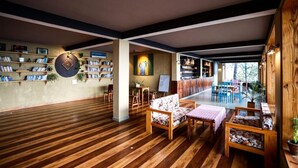 Una habitación amplia con suelo de madera, un área de estar central con una mesa y sillas, y una estantería llena de libros.