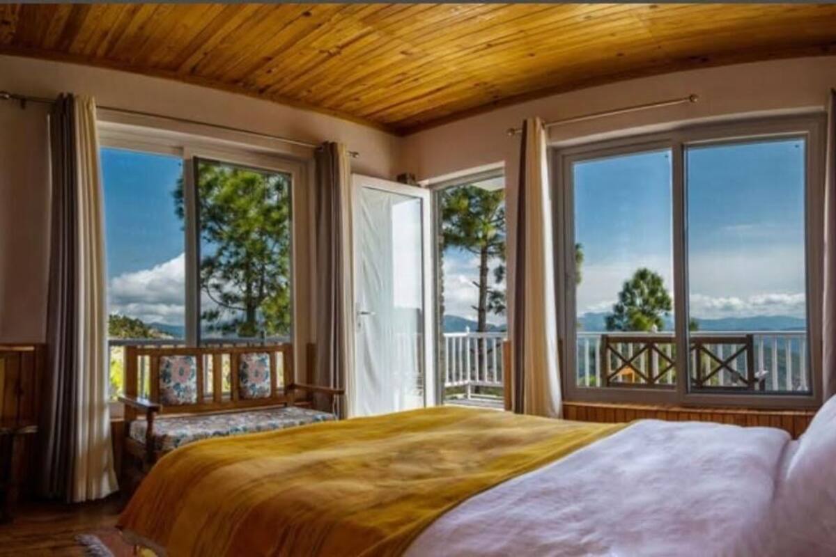 Une chambre avec un grand lit, un balcon doté d’une balustrade et une vue sur les arbres et les montagnes.