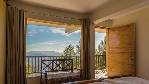 Un dormitorio con una cama grande, un banco de madera y vistas a las montañas desde un balcón.