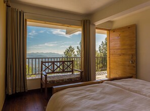 A bedroom with a large bed, a wooden bench, and a view of mountains through a balcony. - Kasar Rainbow Yoga Retreat (Almora)
