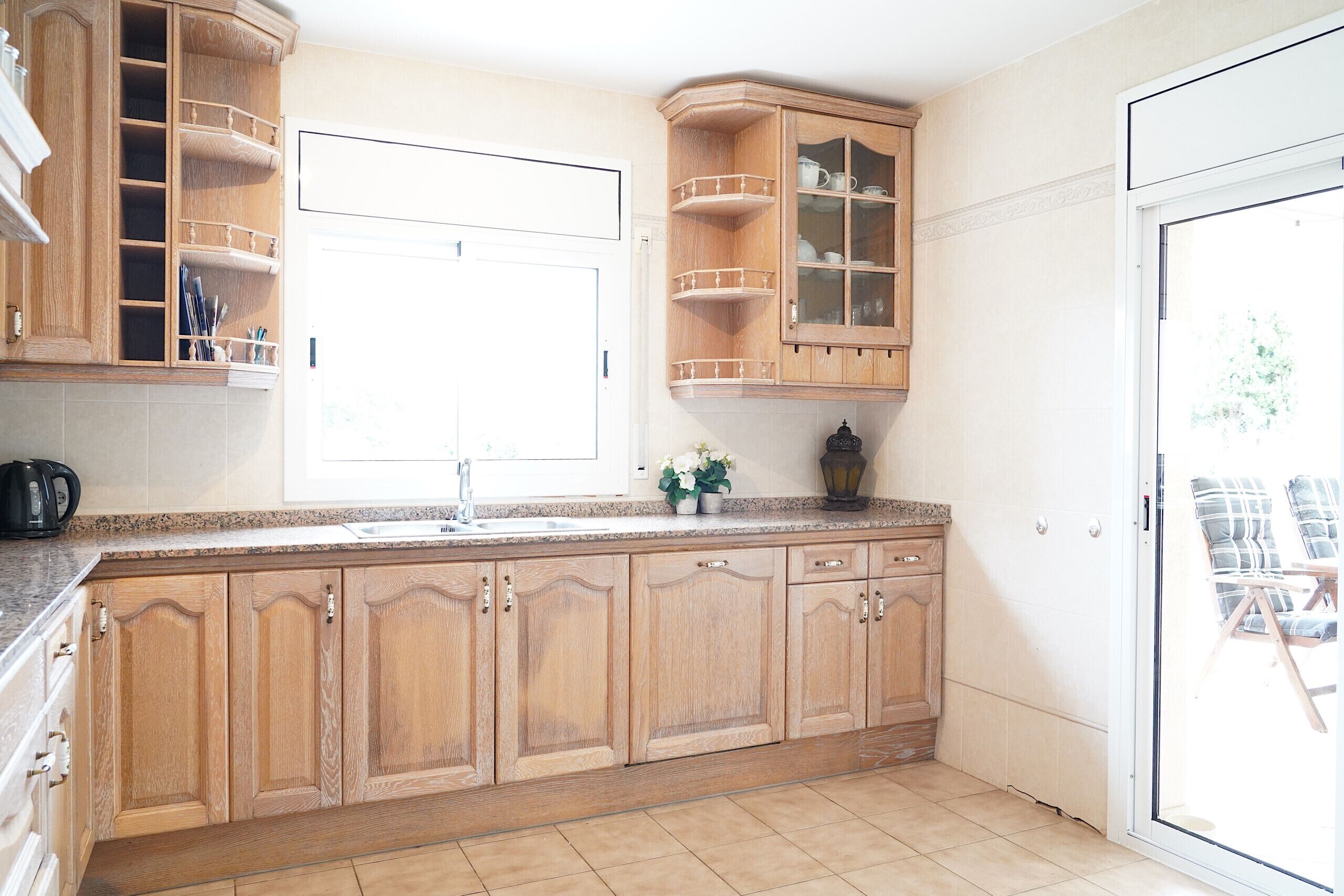 Une cuisine dotée de meubles en bois, d’un plan de travail en granit, d’une fenêtre et d’une porte-fenêtre coulissante donnant sur un espace extérieur.
