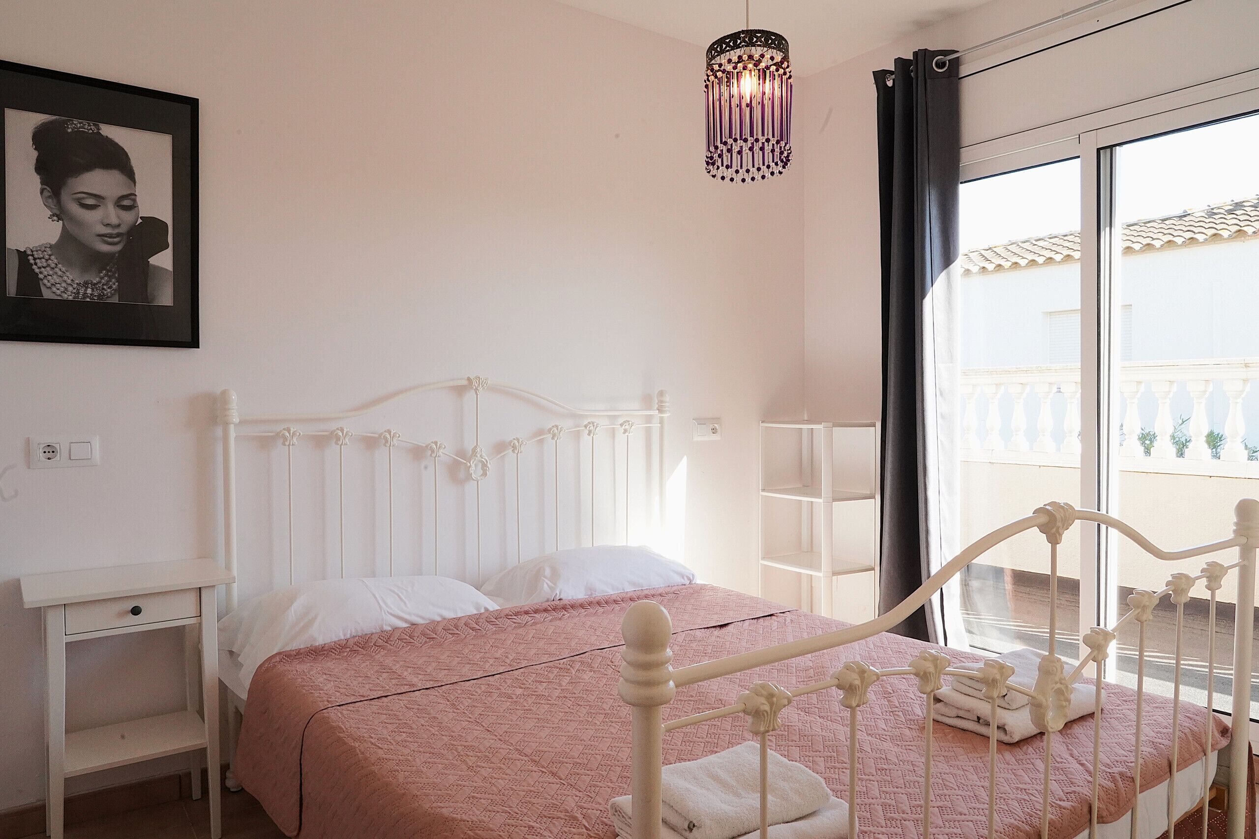 A neatly arranged bedroom with a bed, bedside table, and a hanging light fixture.