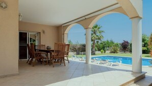 A covered outdoor area with a pool, wooden furniture, and a view of the pool and greenery. - Spacious, good located villa in Sant Pere Pescador (Sant Pere Pescador)