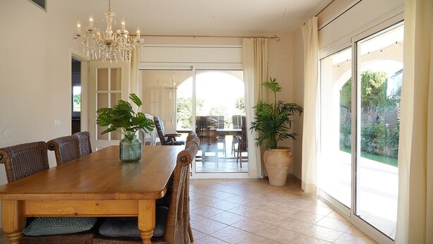 A dining area with a wooden table, wicker chairs, a chandelier, and large windows. - Spacious, good located villa in Sant Pere Pescador (Sant Pere Pescador)