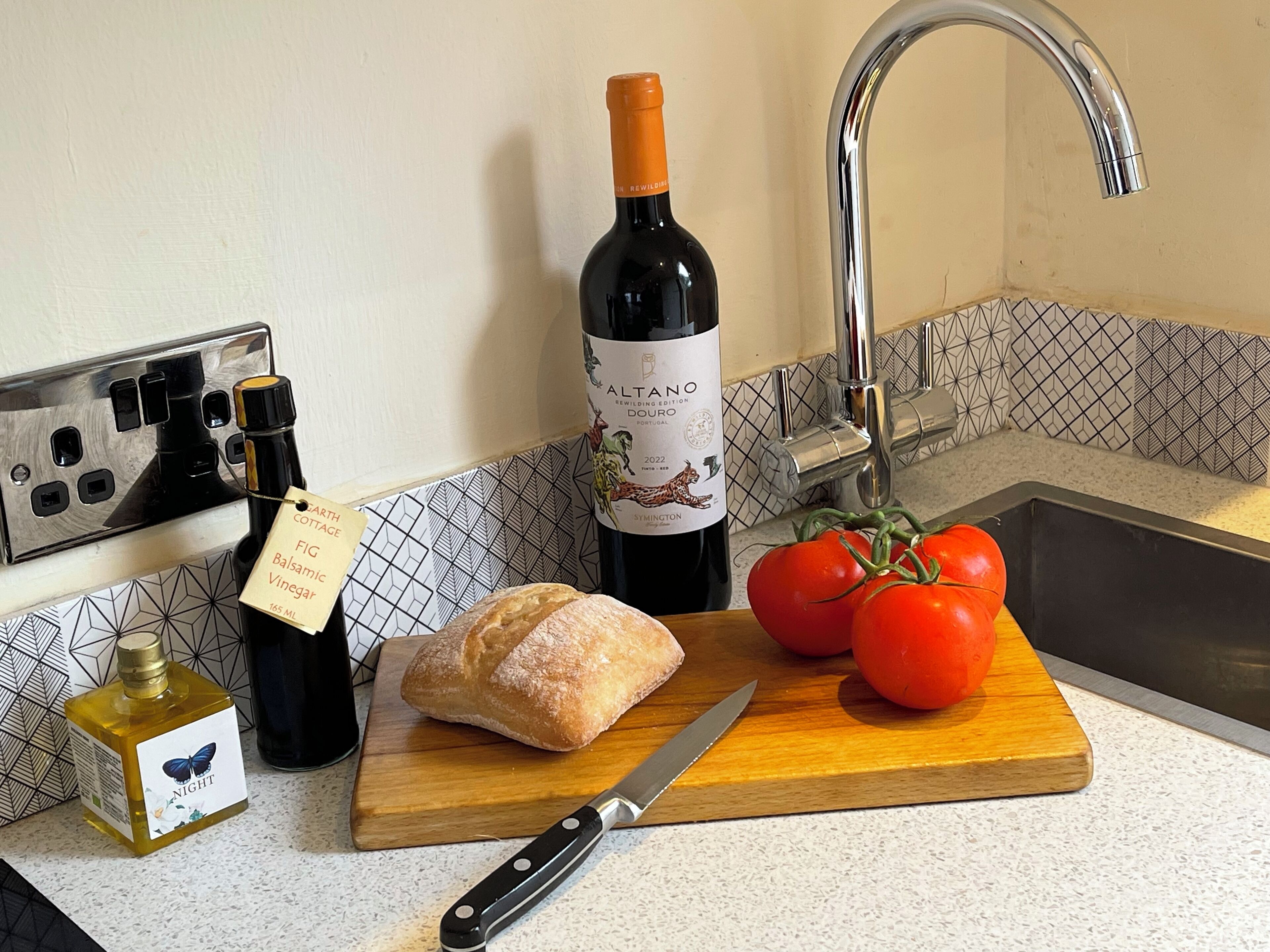 Un comptoir de cuisine avec une bouteille de vin, une miche de pain et des tomates.