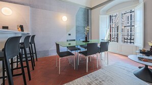 Un coin repas avec une table et des chaises en verre, un sol carrelé de carreaux rouges et une vue dégagée sur l’extérieur grâce à une grande fenêtre.