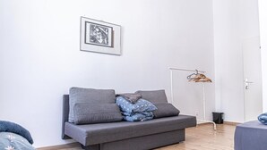 Habitació minimalista amb un sofà gris, un quadre al mur, una làmpada de peu i un sòl de fusta.