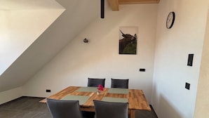 A dining area with a wooden table and four chairs, a clock on the wall, and a ceiling light fixture. - NEW: Cozy vacation apartment in Aidling am Riegsee with mountain views (Riegsee)