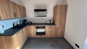 A compact kitchen with wooden cabinets, a black countertop, a built-in oven, and a small window above the sink. - NEW: Cozy vacation apartment in Aidling am Riegsee with mountain views (Riegsee)