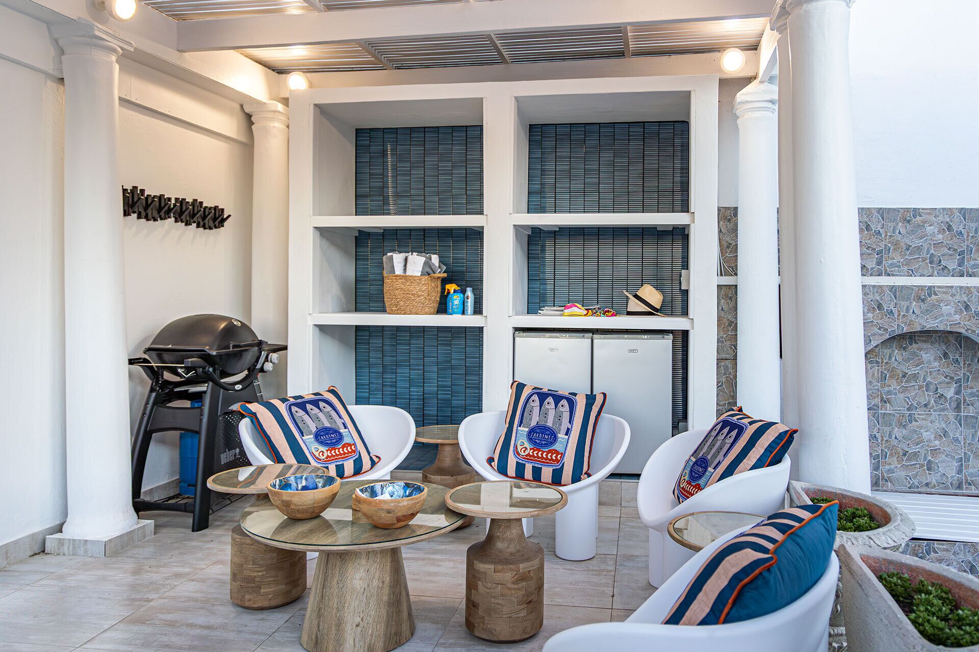 Een moderne buitenruimte met witte stoelen en ronde tafels, een barbecue en een stenen muur.