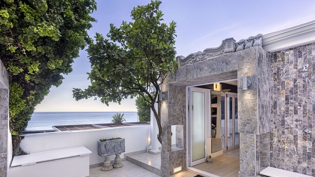 A modern outdoor area with a stone wall, a bench, and a door leading to an interior space. - YOLO Spaces - Clifton Petite Villa (Cape Town)