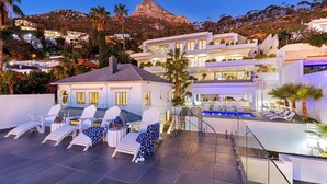 A modern resort with a rooftop pool, lounge chairs, and a view of the surrounding hills. - YOLO Spaces - Clifton Petite Villa (Cape Town)