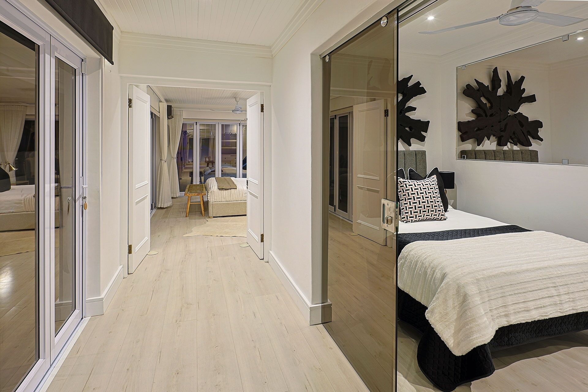 A modern bedroom with a large bed, a glass door leading to a balcony, and a hallway with a chair and a small table.